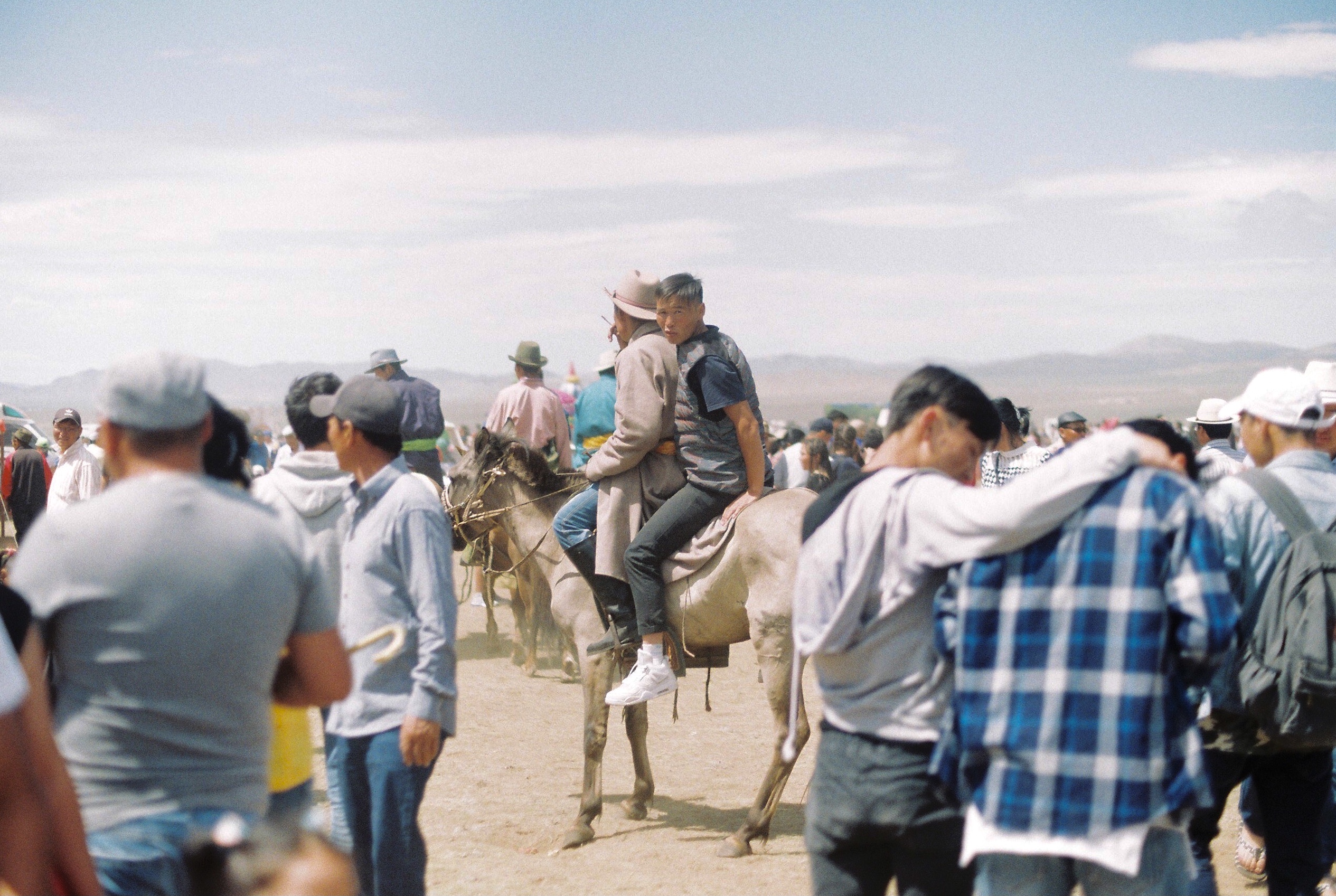 two men sitting on a horse in the middle of a crowd